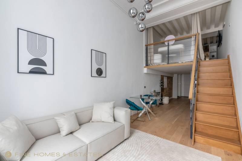 Séjour lumineux en double hauteur révélant mezzanine élégante, volumes remarquables et rénovation soignée, signature d’une agence immobilière Paris 6.